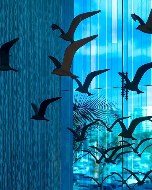 Black bird silhouettes fly past a blue, vertical-striped wall, creating a dramatic futuristic city scene with glass reflections.