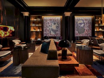 A luxury lounge with velvet seating, glass coffee tables, lit candles, wall maps, and warm lighting like an upscale bar area.
