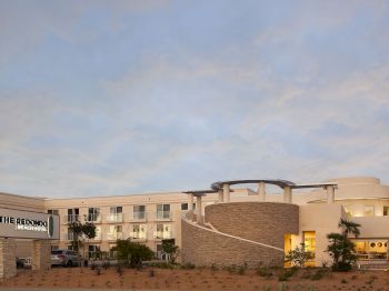 Exterior of The Red Door Beach Hotel building with balconies, a covered entry, and a cloudy sky.