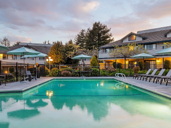 An outdoor hotel pool with lounge chairs and colorful umbrellas, surrounded by houses and trees at sunset.