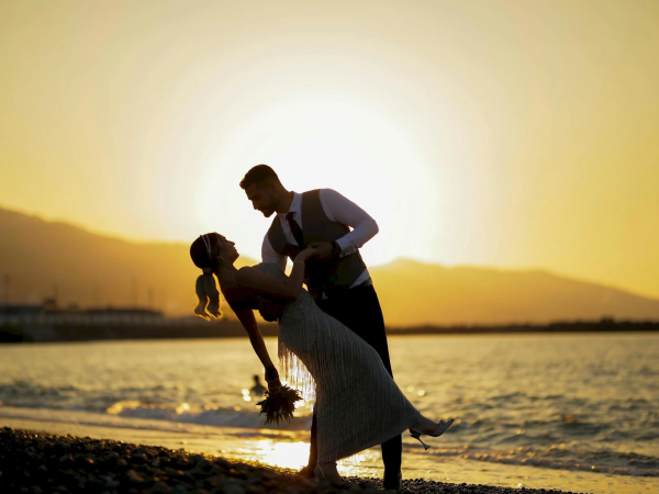 A couple shares a romantic dance on a beach at sunset, silhouetted against the golden horizon.