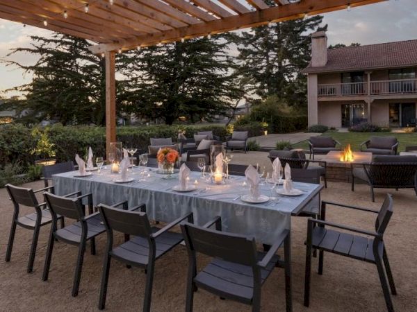 An outdoor patio set for a dinner or wedding: tables with candles and floral centerpieces, chairs, and a fire pit.