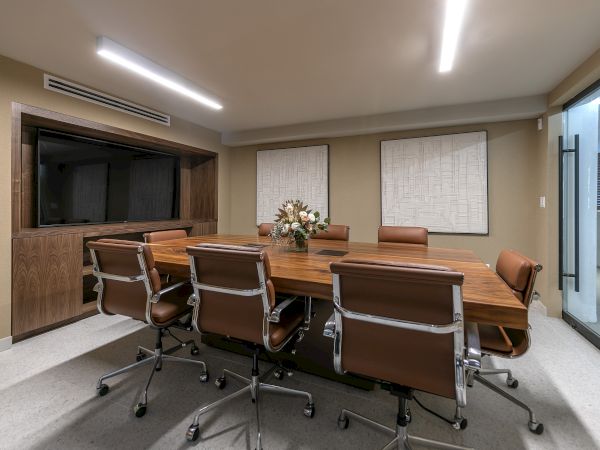 A modern conference room with a long wooden table, leather chairs, wall art, and bright ceiling lights.