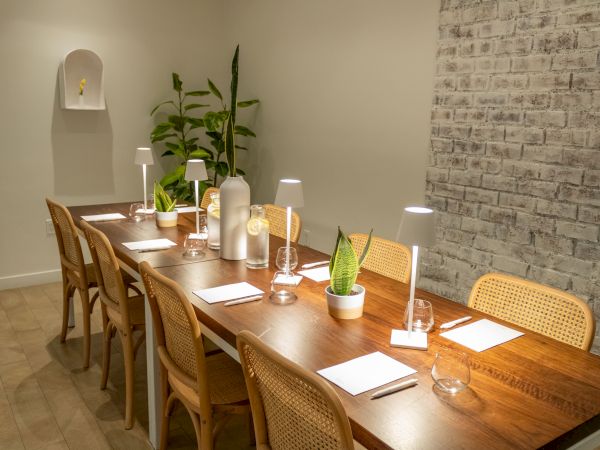 A stylish dining room with a wooden table set for guests, candles and plants, and a brick wall backdrop.
