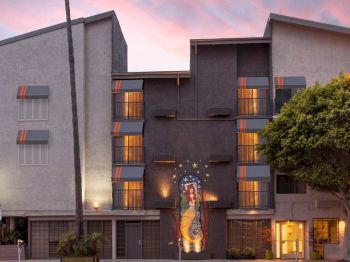 An urban hotel facade at sunset with a mural of a woman holding a staff and starry decorations between balconies.