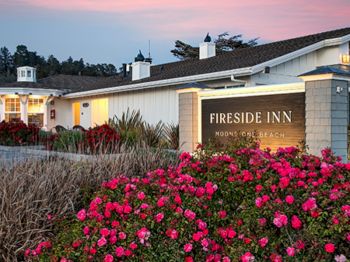 A &ldquo;Fireside Inn&rdquo; sign beside a building, surrounded by colorful pink flowers and shrubs at sunset.