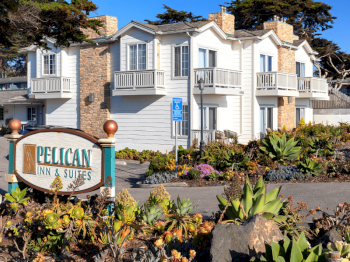 A &ldquo;Pelican Inn & Suites&rdquo; sign stands by a white two-story hotel with stone chimneys and colorful landscaped gardens.
