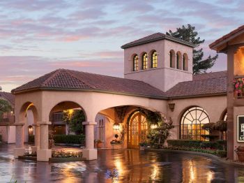 A glowing stucco courtyard with arched hallways, a central entry, and wet stone reflecting lights at dusk.