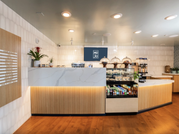 Inside a modern coffee shop, with a marble counter, menu board, espresso machines, and pastries on display.