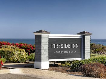 A &ldquo;Fireside Inn&rdquo; sign at Moonstone Beach with colorful flowers and the ocean horizon in the background.
