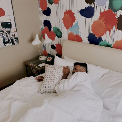 A child lies in bed in a colorful room with a colorful splatter wall design behind them.