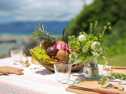 An outdoor lakeside picnic table with fresh flowers in vases and glasses set on a striped blanket.