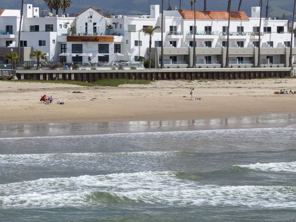 A sandy beach with gentle waves, beachgoers relaxing, and white hotel buildings with palm trees lining the shoreline.