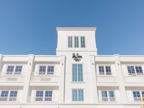 A white building facade with balconies and the &ldquo;Bay Shore Inn&rdquo; sign against a clear blue sky.