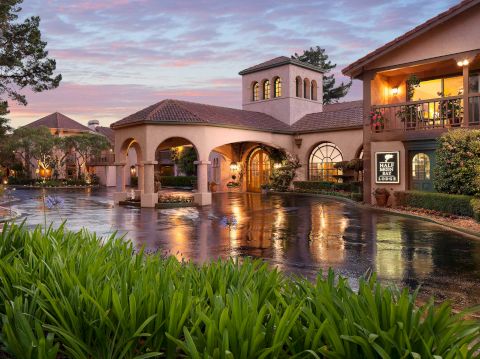 A courtyard pool at dusk outside Half Moon Bay Lodge, with arched buildings, warm lights, flowers, and reflections on still water.